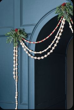 a blue door decorated with white and red flowers, greenery and beads hanging from it's side