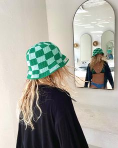 a woman wearing a green and white checkered hat looking at herself in the mirror