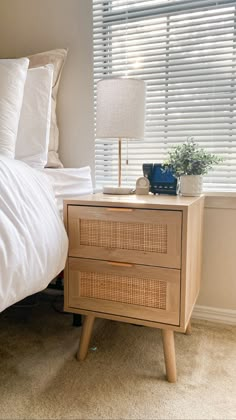 a bed with white sheets and pillows next to a wooden night stand on top of a carpeted floor