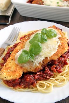 a white plate topped with pasta and meat covered in sauce on top of a wooden table