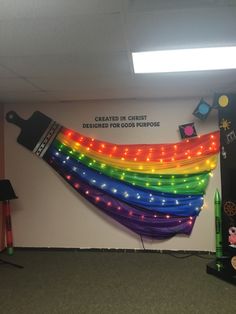 a room with a rainbow colored wall hanging from it's ceiling and lights on the walls