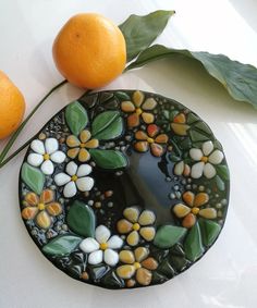 two oranges sitting next to a plate with flowers and leaves painted on it,