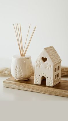 a small white house next to a cup with sticks in it on a wooden tray