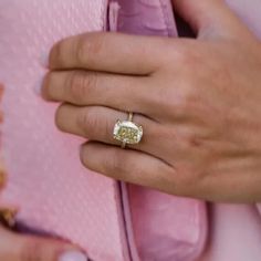 a close up of a person's hand with a ring on their finger and a pink purse in the background