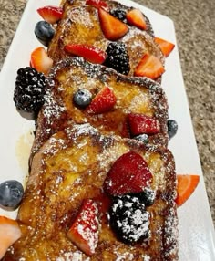 french toast with berries and powdered sugar on a white plate sitting on a counter