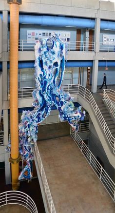 a large blue and white sculpture hanging from the side of a building next to stairs