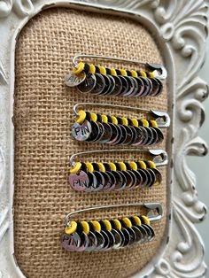 four yellow and black pins sitting on top of a piece of fabric next to a white frame