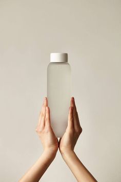 two hands holding up a white bottle in the air