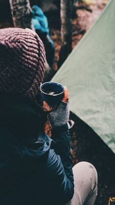 a person sitting in the woods holding a cup with their hand up to their face