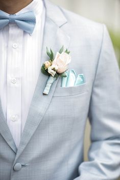 a man wearing a blue suit and bow tie with a boutonniere on his lapel