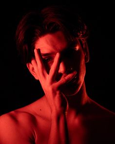 a shirtless man holding his hand to his face in the dark with red light