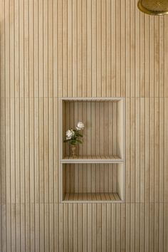 an empty shelf in the corner of a tiled wall with a vase and flowers on it