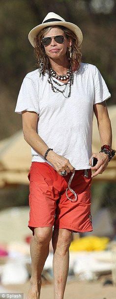 a man walking on the beach wearing red shorts and a hat