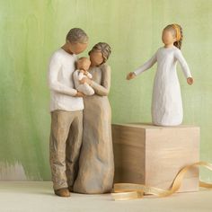 a figurine of two people holding a baby next to a box with a ribbon on it