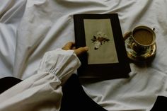 a person is holding an open book with flowers on it and a cup of coffee