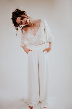 a woman wearing white pants and a cropped top is posing for the camera with her hands on her hips