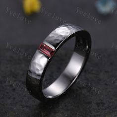 a wedding ring with two red stones in it on top of a black table next to flowers