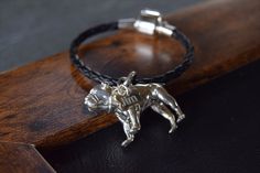 a silver dog charm sitting on top of a black leather bracelet with a wooden box in the background