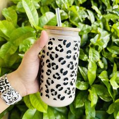 a hand holding a coffee cup with a straw in front of some bushes and plants