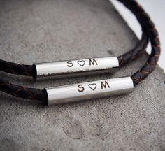 two personalized leather bracelets with hearts on them sitting on top of a rock