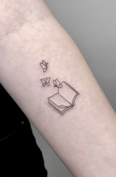 a woman's arm with a book and butterflies tattoo on the back of her left arm