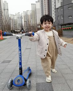 a small child is standing next to a scooter on the sidewalk with buildings in the background