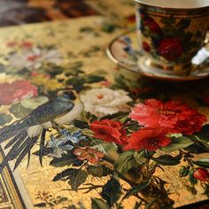 a coffee cup sitting on top of a table next to a plate with flowers and birds