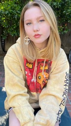 a woman sitting on top of a blue bench wearing a yellow hoodie and earrings