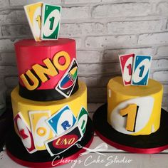 two tiered cake decorated with uno and uno signs on each layer, sitting next to each other