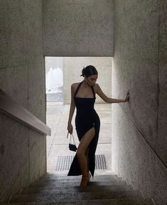 a woman in a black dress is walking down some stairs with her hand on the wall