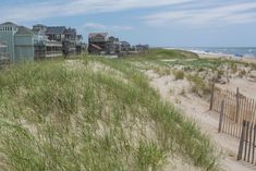 the beach has grass growing on it and houses in the background, along with sand dunes