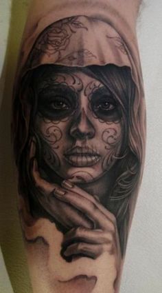 a woman's face painted with black and white sugar skull tattoos on her leg