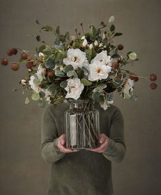 a person holding a vase filled with flowers and greenery in front of their face