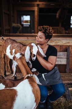 a woman petting two goats in a barn