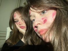 two girls with their faces painted pink and blue are looking at the camera while standing in front of a mirror