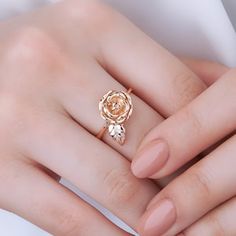 a woman's hand wearing a gold ring with a rose on the center and leaves around it