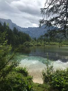 a lake surrounded by trees and mountains in the distance with water running down it's sides