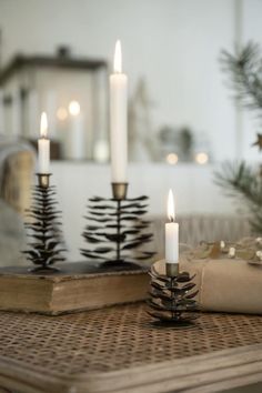 three lit candles are sitting on a table next to an open book and christmas tree