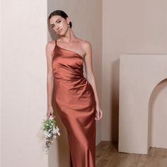 a woman in an orange dress standing next to a white wall and holding a bouquet