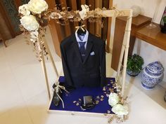 a suit and tie on display in front of a blue table with white flowers, vases and other items