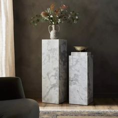 two marble vases with flowers in them sitting on a table next to a chair