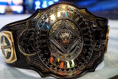 a close up of a wrestling belt on a white surface with red lights in the background