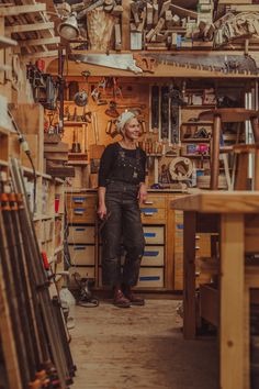 a woman standing in a workshop with lots of work on the wall and shelves full of tools