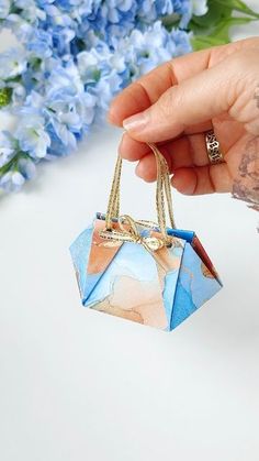 a hand holding a small origami bag next to some blue and white flowers