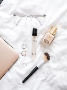 an open laptop computer sitting on top of a bed next to makeup and eyeglasses