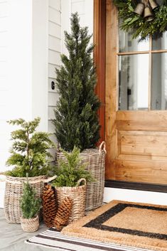 three baskets with christmas trees in them sitting on the front door step next to a welcome mat