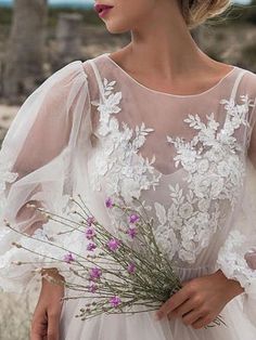 a woman in a white wedding dress holding a bouquet of flowers and looking off into the distance