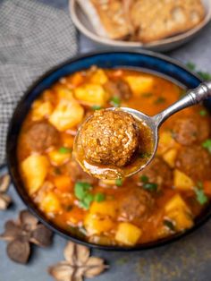 a spoon full of meatball soup with bread on the side