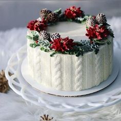 a white frosted cake with pine cones and poinsettis sitting on a plate