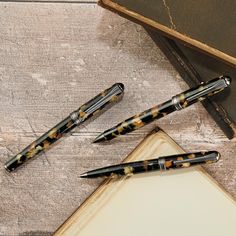 three pens sitting on top of an open book next to a pen and paper pad